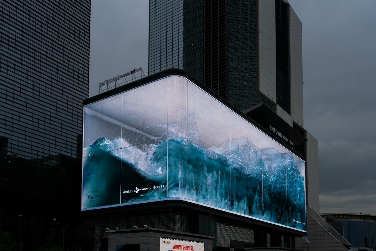 A large digital screen displays a teal wave on a skyscraper.